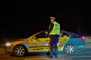 Zdjęcie przedstawia policjanta Wydziału Ruchu Drogowego, który dokonuje badania stanu trzeźwości kierującego taksówką.