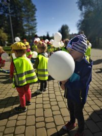 Dzieci w odblaskowych kamizelkach wraz z balonami.