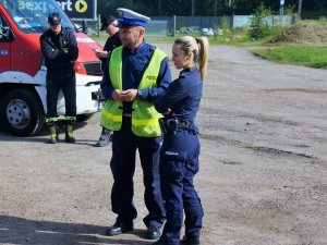 policjantka i policjant w mundurach policyjnych stoją obok, w tle strażacy i strażacki pojazd