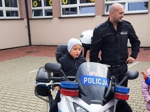 chłopczyk siedzi na policyjnym motocyklu, obok stoi policjant z drogówki i się uśmiecha