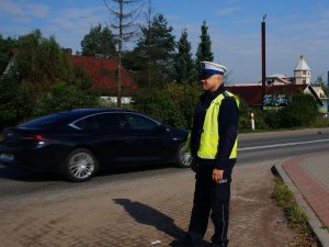 policjant w mundurze i policyjnej czapce przygląda się przejeżdżającym pojazdom