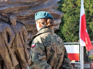 Żołnierka stoi na tle flagi Polski i pomnika Bohaterów Powstań Śląskich