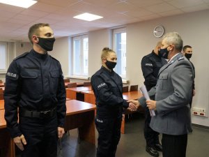 Policjanci stoją obok siebie w szeregu, Komendant wręcza policjantce akt ślubowania, Komendant ściska dłoń policjantce