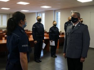 policjanci stoją w szeregu, przed nimi stoją naprzeciwko siebie policjantka i Komendant, policjantka składa meldunek