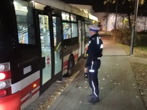 policjant czeka przed autobusem komunikacji miejskiej, stoi na wysokości tylnych drzwi wejściowych, oczekuje na pasażerów, którzy będą wysiadali