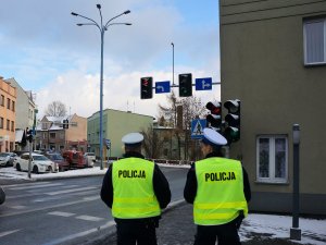 funkcjonariusze w policyjnych mundurach stoją tyłem, obserwują ruch pojazdów w rejonie skrzyżowania