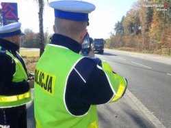 policjanci drogówki obserwują ruch na drodze, jeden z policjantów mierzy urządzeniem do pomiaru prędkości prędkość pojazdu