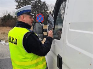 umundurowany policjant przekazuje pakiet z gadżetami zatrzymanemu do kontroli drogowej kierowcy busa