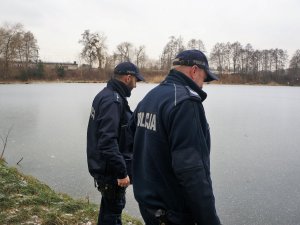 dwaj dzielnicowi stoją przy zbiorniku wodnym, sprawdzają stan pokrywy lodowej