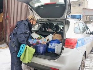 policjantka wyjmuje z bagażnika radiowozu koce dla bezdomnych zwierząt