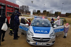 Zdjęcie przedstawia grupę dzieci oglądających policyjny radiowóz. Obok stoi wóz strażacki.