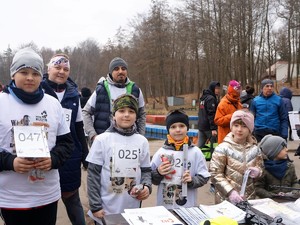 do zdjęcia pozują dzieci oraz dorośli, na sobie mają koszulki z logo imprezy sportowej i numery startowe na klatce piersiowej. W rękach trzymają odblaski.