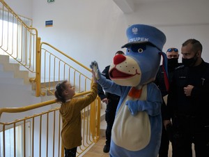 na klatce schodowej dziewczynka przebija piątkę Sznupkowi, obok stoją dwaj policjanci