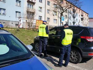 policjanci kontrolują pojazd, który stoi zaparkowany na miejskim parkingu samochodowym, na pierwszym planie widać policyjny radiowóz