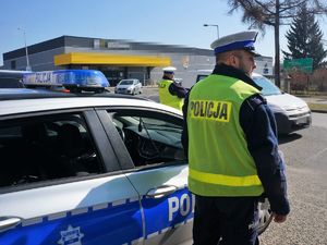 policjant stoi przy radiowozie zaparkowanym na parkingu, obserwuje ruch pojazdów