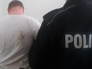 policjant stoi tyłem z zatrzymanym mężczyznom. Widać część policyjnego polaru i sylwetkę zatrzymanego