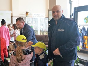 policjant stoi obok dzieci, które mają na głowach odblaskowe czapki