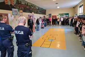 Dwaj umundurowani policjanci stoją przed grupą młodzieży na szkolnym korytarzu