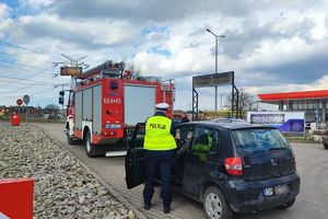 Na parkingu samochodowym policjant rozmawia z kierowcom zatrzymanego pojazdu, który siedzi za kierownicą, przed zatrzymanym pojazdem stoi wóz strażacki