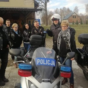 kobiety i mężczyźni stoją obok policyjnego motocykla, obok nich stoi policjant, na głowie ma założony kas motocyklowy