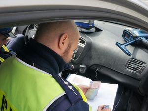 policjant siedzi w radiowozie i spisuje do swojego notatnika dane z dokumentów kierowcy