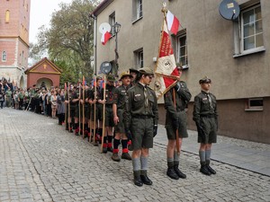 na uliczce między kamienicami stoją harcerze w mundurach, ustawieni w rzędach 4- osobowych