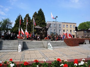 przed Pomnikiem Powstańców Śląskich trwają uroczystości, pomnik jest ozdobiony kwiatami w barwach narodowych