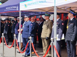 w rzędzie stoją funkcjonariusze różnych formacji ubrani w stroje galowe. Oficer Policji oddaje honor.