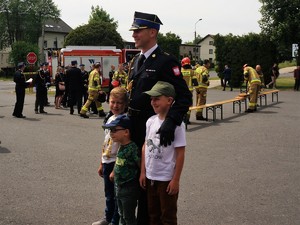 Strażak w mundurze galowym pozuje do zdjęcia z trzema chłopcami