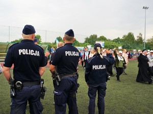 po boisku maszerują uczestnicy XVIII Powiatowej Olimpiady Osób Niepełnosprawnych, na pierwszym planie, tyłem do zdjęcia stoją 2 policjanci i policjantka, która macha ręką do uczestników