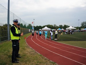 na bieżni sportowej, uczestnicy XVIII Powiatowej Olimpiady Osób Niepełnosprawnych ścigają się, obok bieżni stoją dwaj policjanci, którzy im kibicują