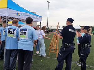 policjant i policjantka stoją przy stanowisku rzutek i kibicują uczestnikowi, który rzuca