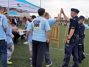 policjant przebija piątkę z uczestnikiem XVIII Powiatowej Olimpiady Osób Niepełnosprawnych, którzy rzucił rzutką do celu, obok policjanta stoi policjantka