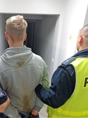 policjant podtrzymuje zatrzymanego mężczyznę, stoją tyłem