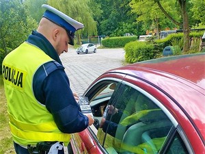 policjant stoi obok pojazdu podczas kontroli drogowej, przekazuje kierowcy ulotkę informacyjną