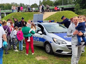 na terenie zielonym stoi zaparkowany policyjny radiowóz, obok stoją dorośli z dziećmi, w tle widać kolorowe namioty i tłum ludzi