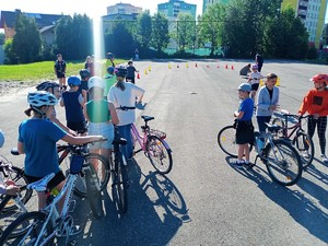na szkolnym boisku, dzieci stoją obok rowerów, przed nimi znajduje się rząd utworzony z pachołków