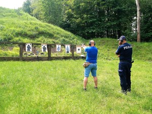 na strzelnicy, nieumundurowany policjant strzela do tarczy, za nim stoi umundurowany policjant, który obserwuje, jak strzela