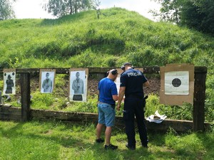 nieumundurowany policjant i umundurowany policjant stoją przy tarczy, obserwują przestrzeliny