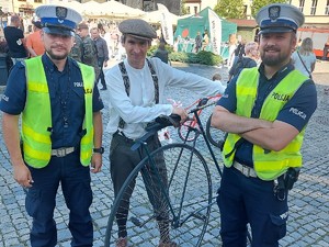 dwaj umundurowani policjanci pozują do zdjęcia z mężczyzną, który trzyma antyczny rower z wielkim tylnym kołem