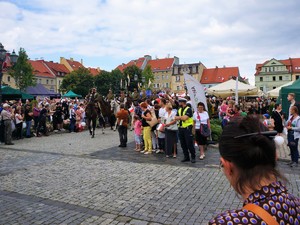 umundurowany policjant stoi obok uczestników uroczystych obchodów na wodzisławskim Rynku, trwa przejazd orszaku, widać mężczyzn z mundurach wojskowych, którzy jadą na koniach