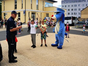 Policjant i Sznupek przyglądają się chłopcu, który strzela z łuku, obok chłopca stoi animatorka i inne dzieci