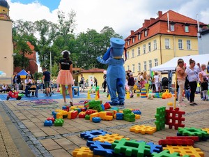 Animatorka i Sznupek stoją do zdjęcia tyłem, w tle znajdują się uczestnicy festynu