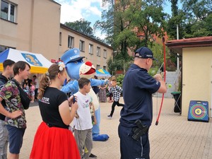 policjant strzela z łuku, animatorka, Sznupek i dzieci przyglądają się policjantowi