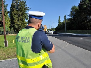 policjant mierzy prędkość pojazdów jadących po drodze