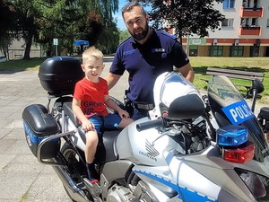 na policyjnym motocyklu siedzi chłopczyk, obok niego stoi policjant w mundurze