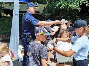 na plaży stoi policjant, rozdaje ulotki dzieciom, które w grupie stoją przed nim