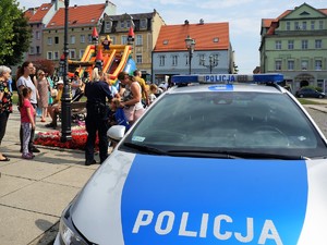 na rynku stoi zaparkowany policyjny radiowóz, obok stoi policjantka i rozmawia z uczestnikami festynu, w tle widać dmuchaną zjeżdżalnię dla dzieci