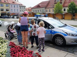 na rynku, obok policyjnego radiowozu stoją dzieci i dorośli, oglądają radiowóz