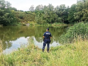 umundurowany policjant stoi przy brzegu zbiornika wodnego